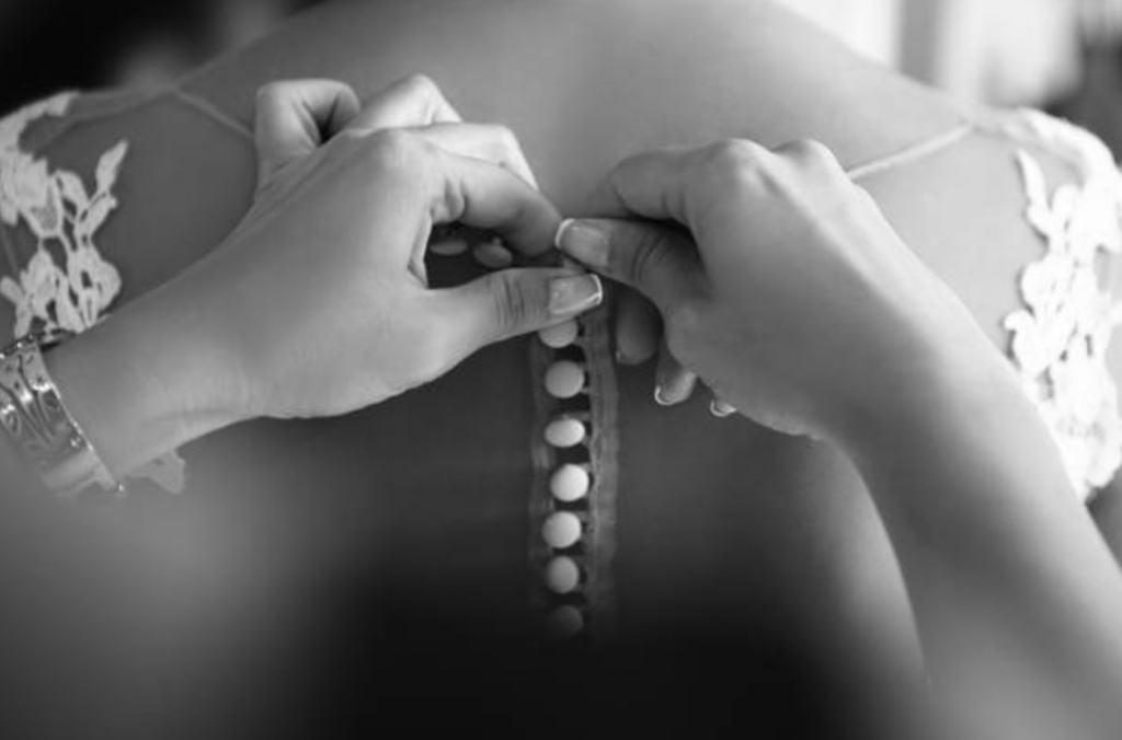 A black and white image of a necklace boing put on a bride | Motif