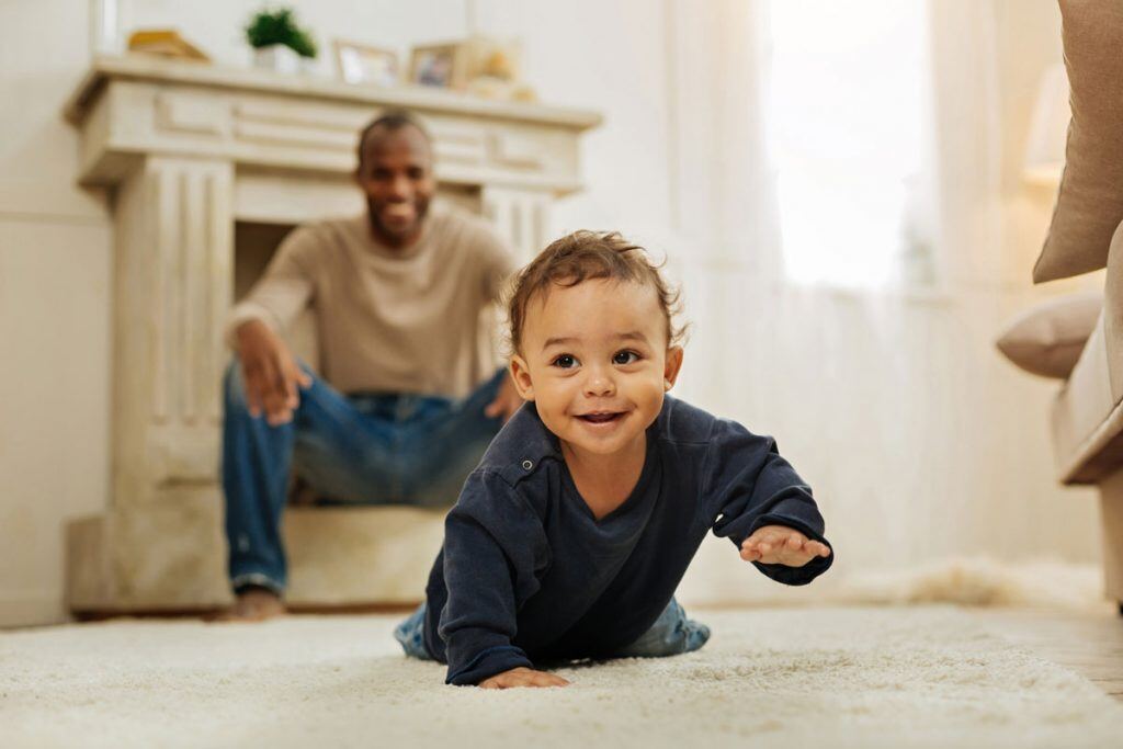 A father sitting down behind his crawling son | Motif