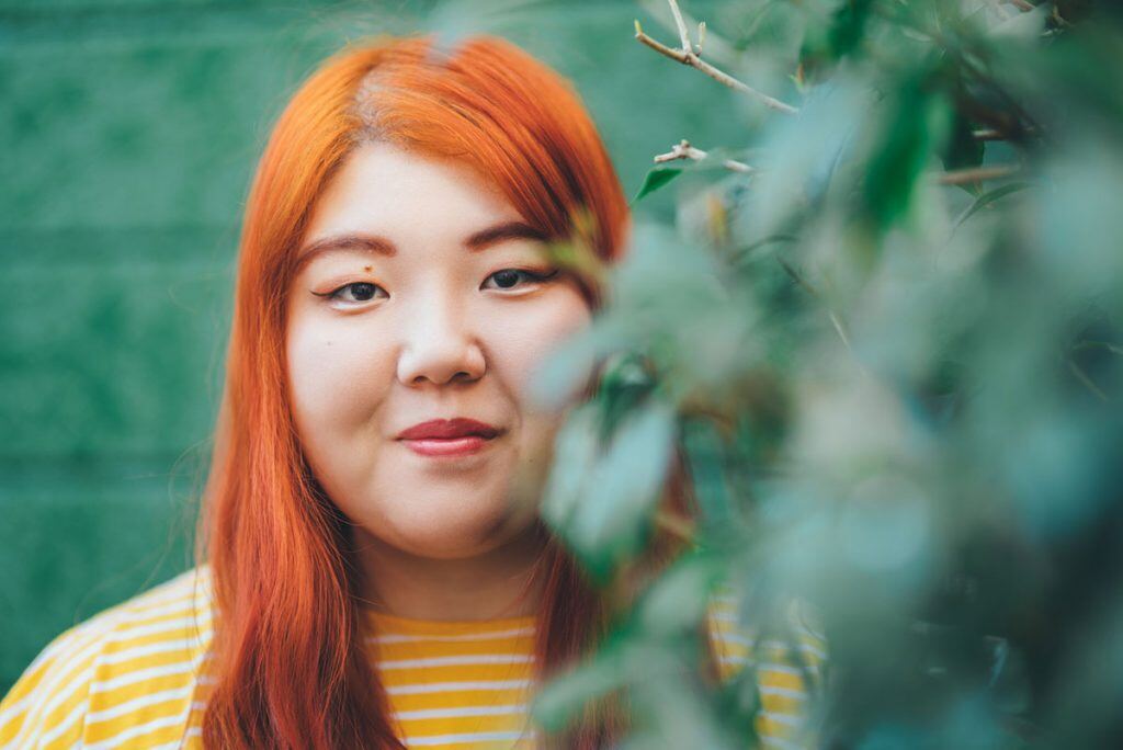 A portrait mode photo of a girl standing in some foliage | Motif