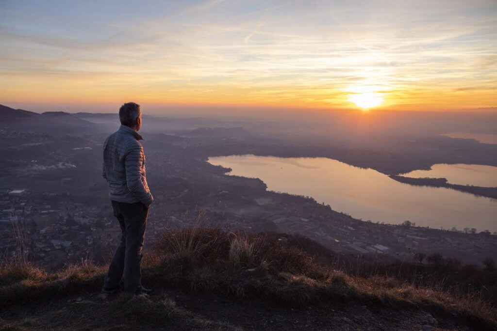 Hiker watches a sunrise at the top of a large hill.