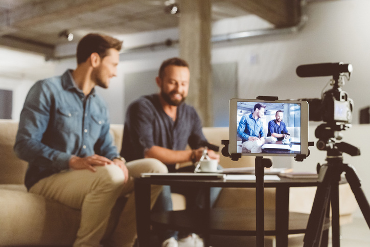 Two guys on a couch, ready to shoot video or photography on iPad with camera stand and mic.