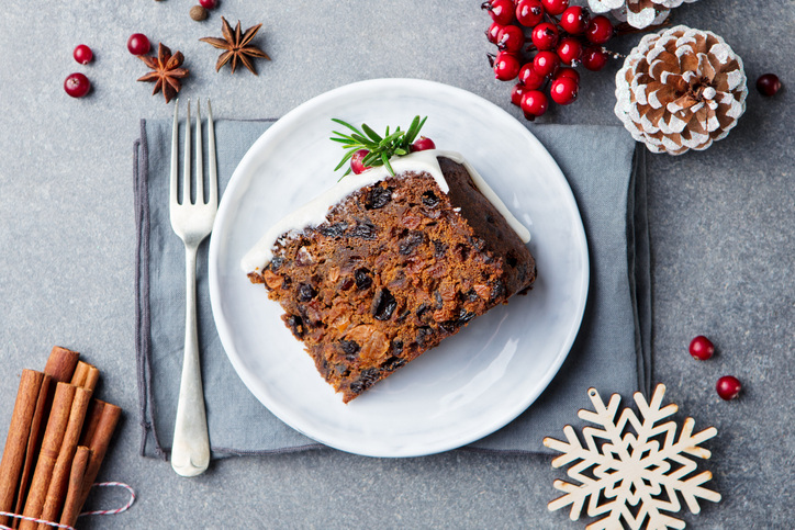 Christmas photography can be a slice of fruit cake on white plate with fork and seasonal décor.