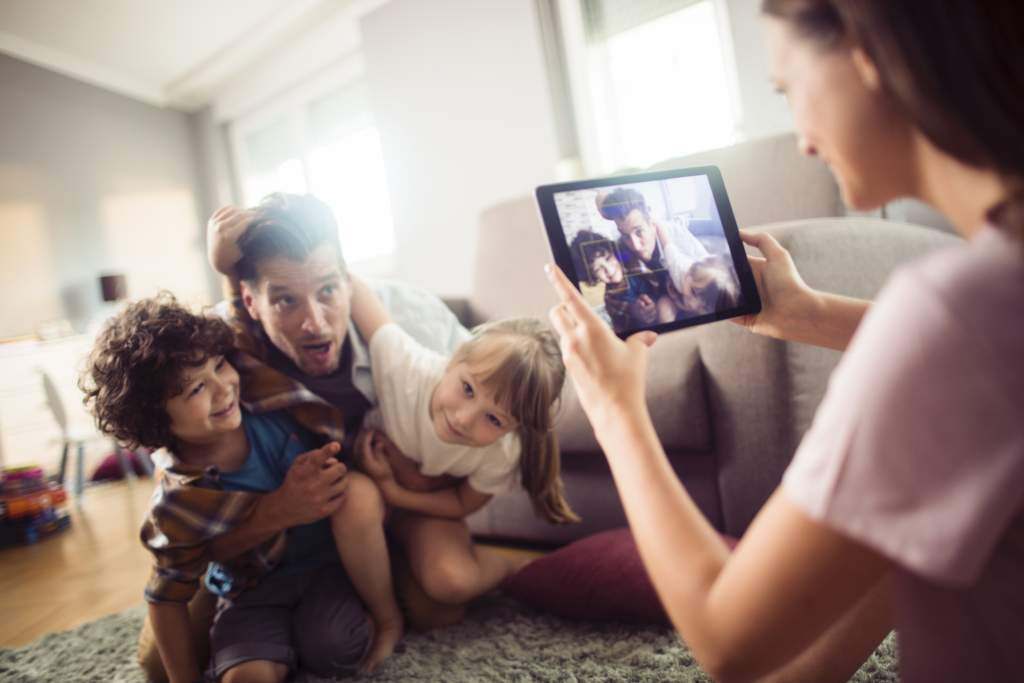 Mom uses an iPad to take photos of dad with two kids playing in JPEG format.