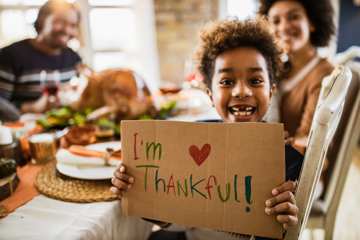 Young girl with “I’m Thankful” sign at dinner table with family, makes cute Thanksgiving pictures.