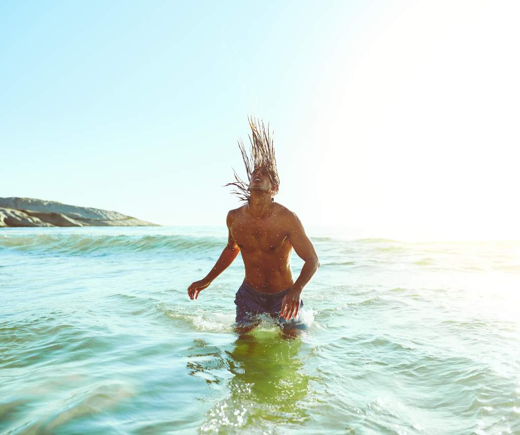 A man in the ocean demonstrates funny poses for pictures by flipping water with long hair.