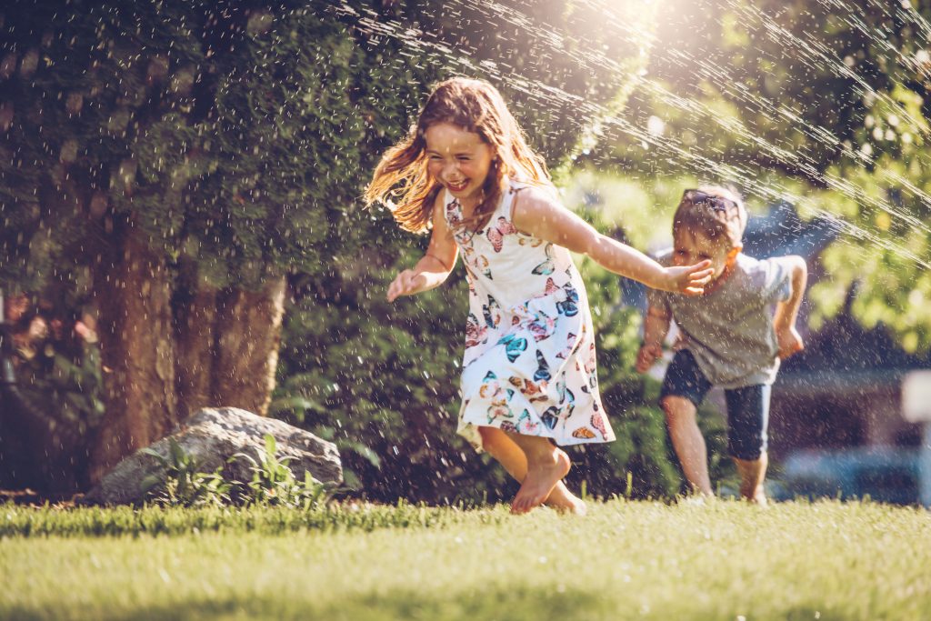 Include two kids running through a sprinkler in your summer photoshoot ideas.