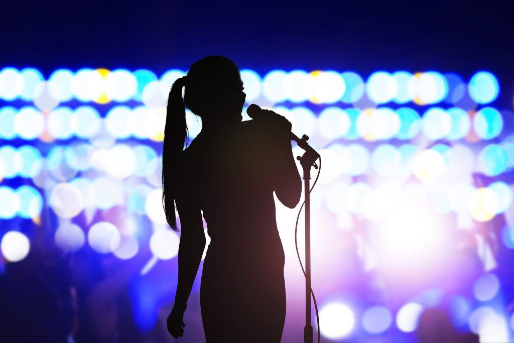 The silhouette of a woman singing creates contrasting color photography against bright lights.