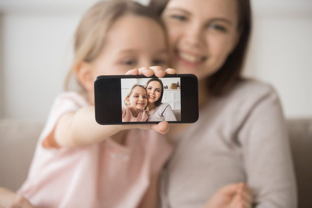 Happy mother and daughter follow key selfie tips by using rear-facing camera to take a quality photo