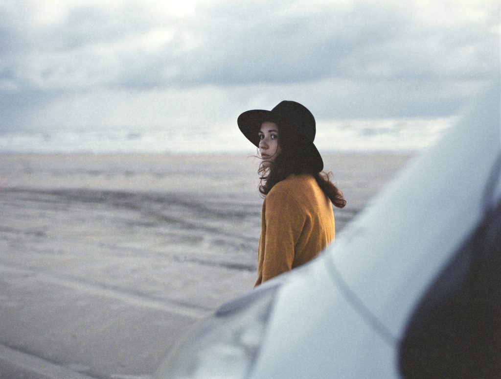 Woman standing by camper wears pumpkin-colored sweater and black hat for contrast.