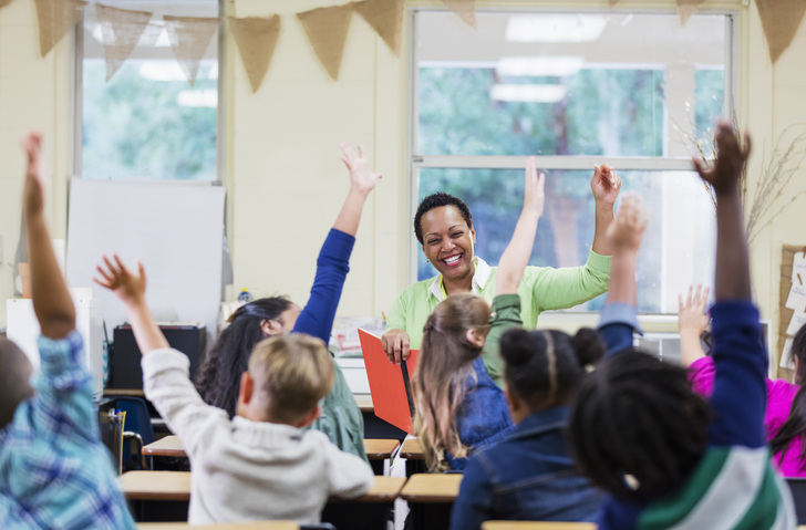 DIY Christmas gift idea: photo book of teacher in front of young kids with hands raised.