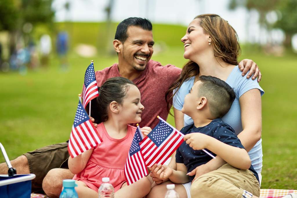 Parents and kids with flags in park celebrate July 4th for their summer family picture.