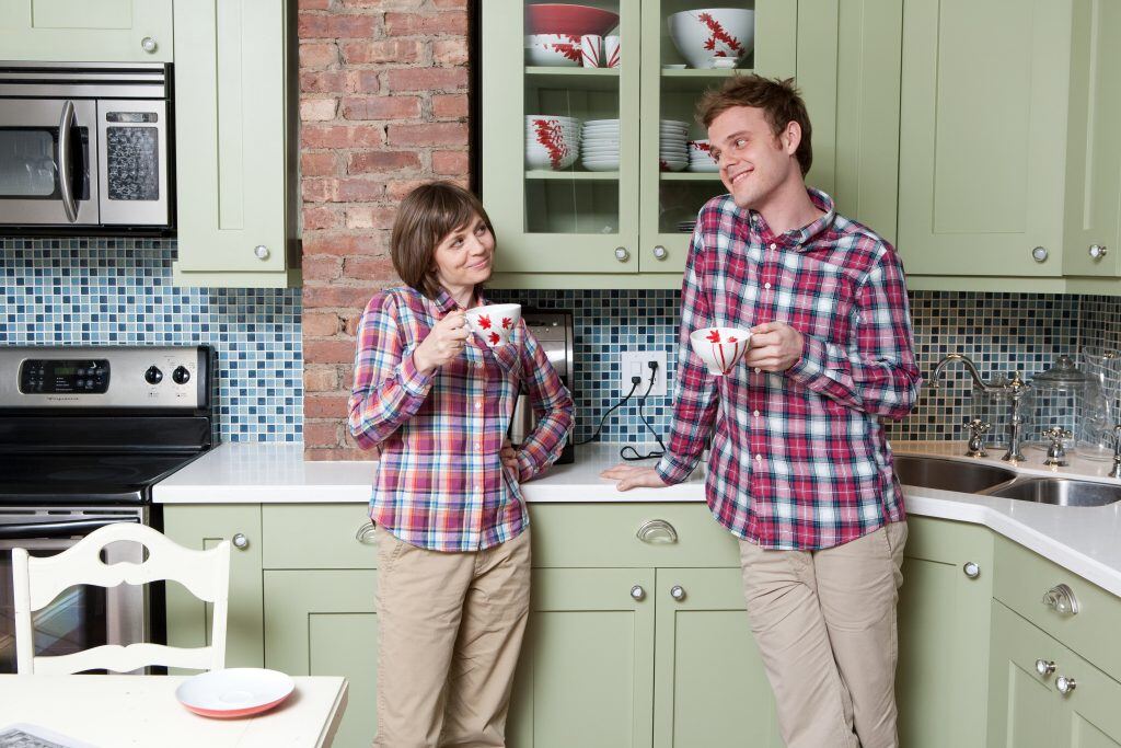 A young couple dressed in matching plaid shirts and khakis take funny selfie pose in the kitchen.