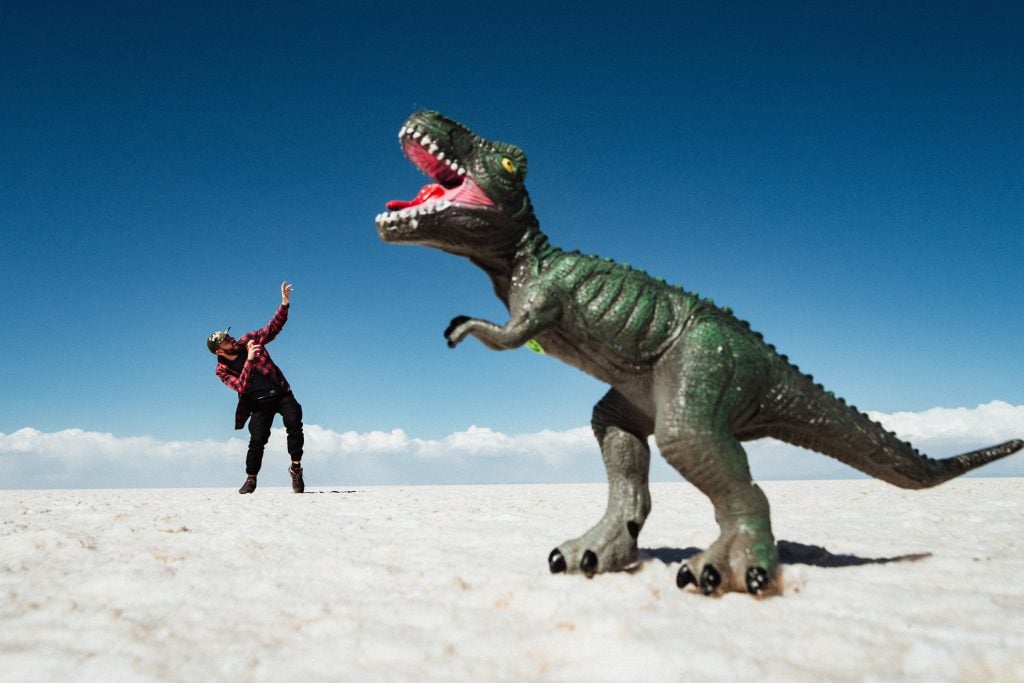 Man creates funny selfie idea, where it looks like toy dinosaur is attacking him outside.