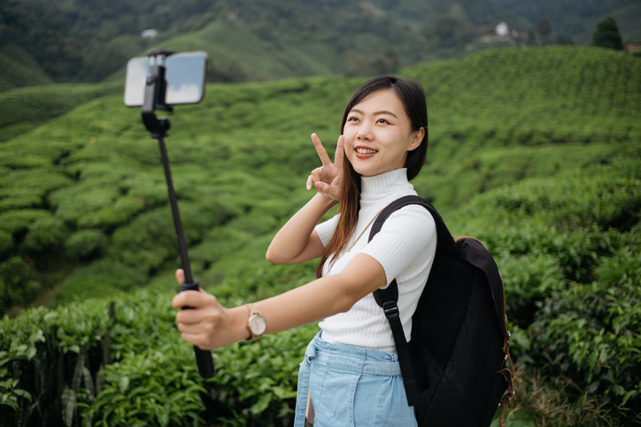 Asian woman holds selfie stick on tea plantation, one of the best photography gifts for level.