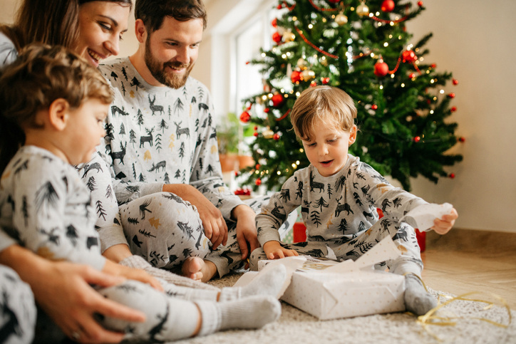 Photo of mom, dad and 2 kids in matching PJs opening presents is cute Christmas card idea.