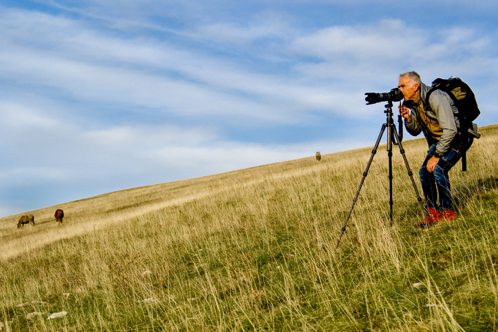 Man uses tripod and telephoto lens in a field, two of the best photography gifts.