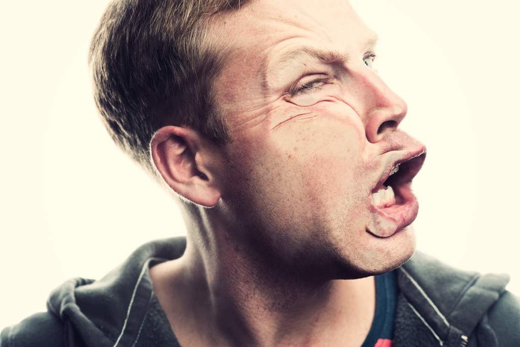 Man presses right cheek against clear glass to squish face and practice funny poses for pictures.