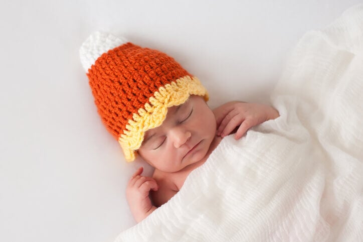 Cute Halloween photoshoot ideas include a sleeping newborn wearing candy corn beanie.