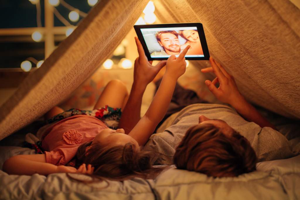 Father and daughter lying in a fort edit selfies to use in their photo book on iPad.