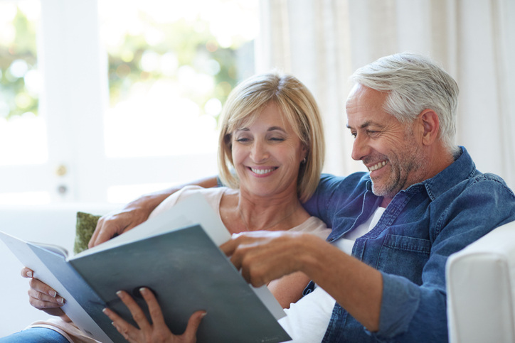 A middle-aged couple sits on couch, flipping through a DIY custom photo book.