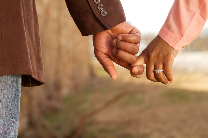 Closeup of African American male and female hands show off new ring in engagement photos.