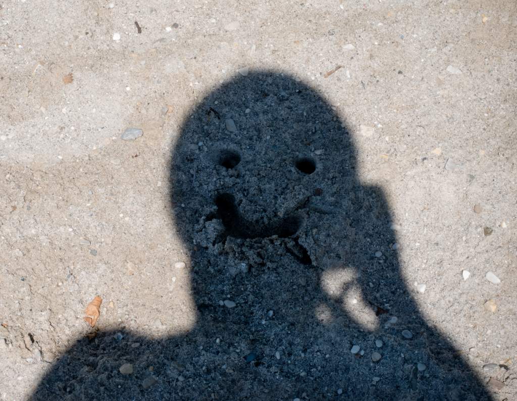 A person’s shadow has eyes and mouth drawn in the sand to make a funny pose for pictures.