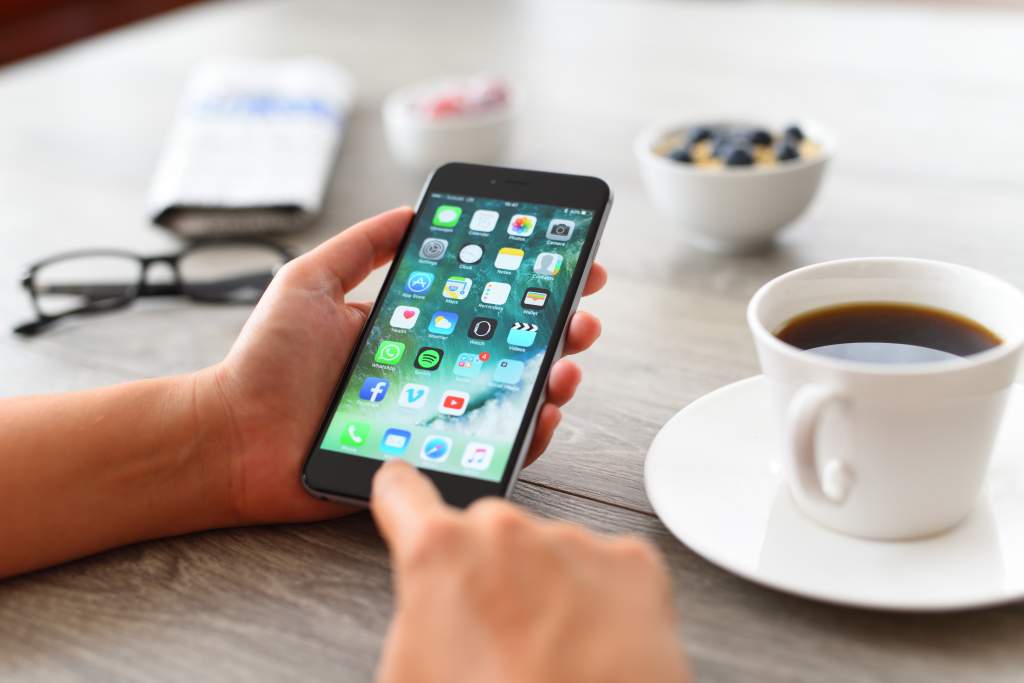 Woman about to tap the iPhone Camera app to take a photo of the coffee cup on her desk.  