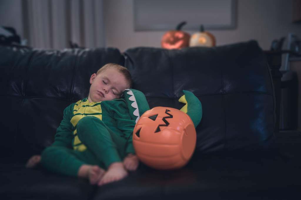 Little boy asleep on couch in dragon costume is the perfect setting for cute Halloween photos.