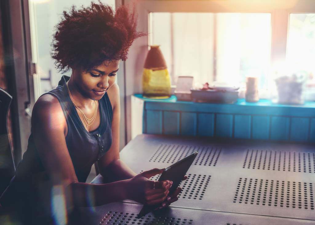 Young black woman sits at the kitchen counter while learning how to convert iPad photos to JPEG.