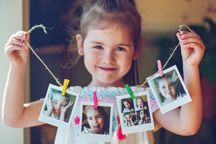 Little girl holds up photography gifts she made of Polaroids on a string.