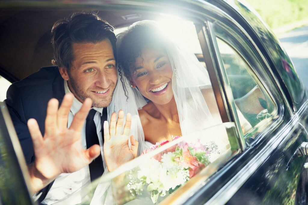 Newlyweds waving from inside a car | Motif