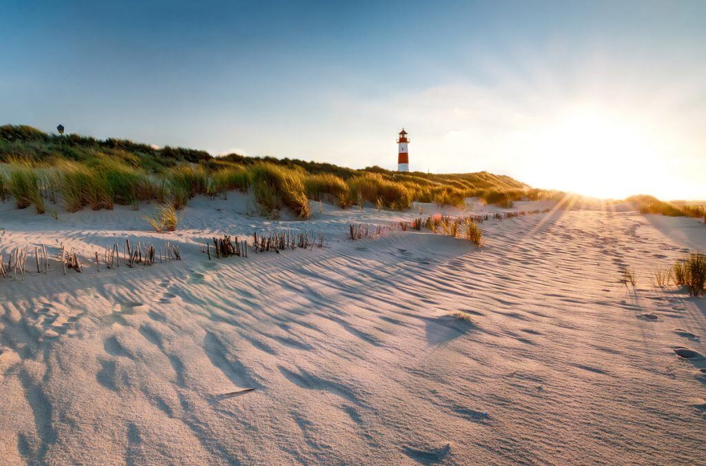 The sun setting behind a beach with a lighthouse | Motif