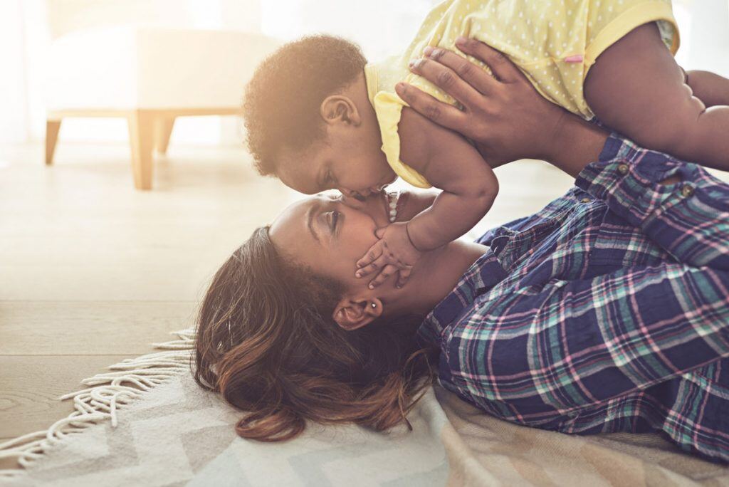 Mom laying on the floor holding and kissing her baby | Motif