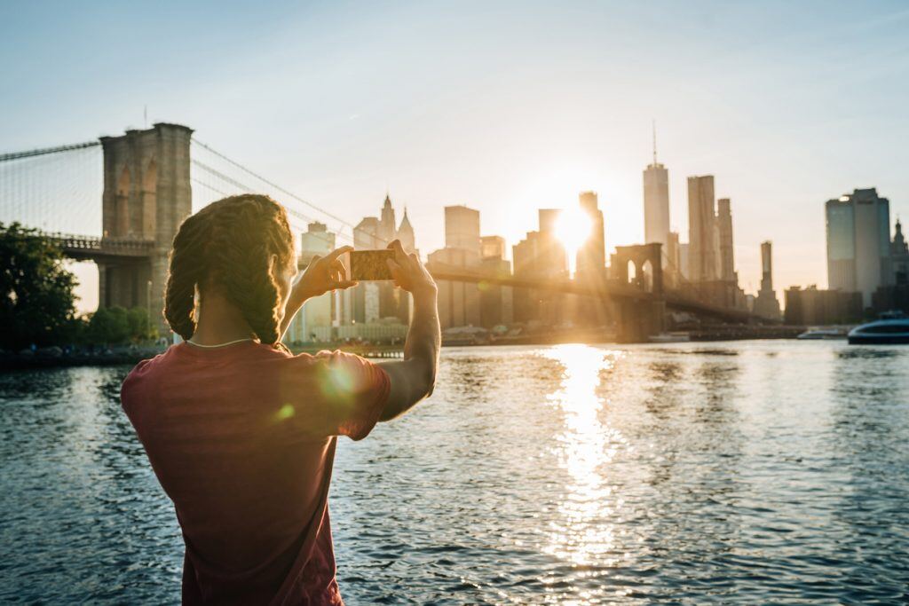 A girl taking a picture of a city with the sun behind the buildings | Motif