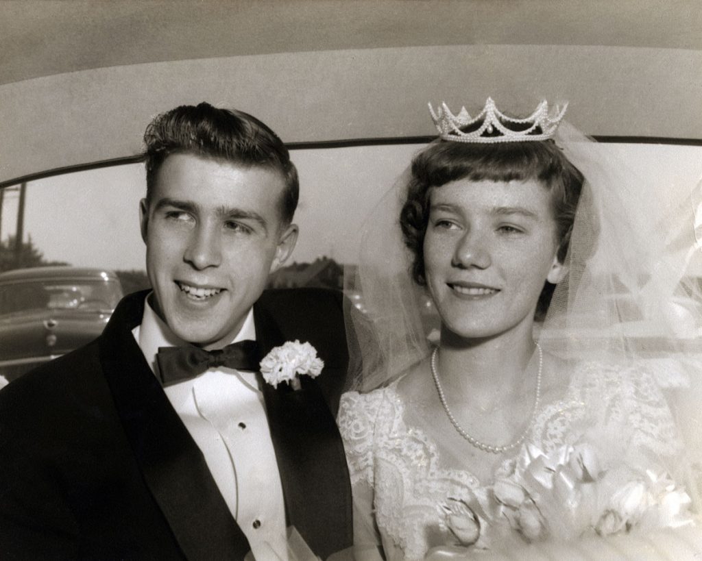 An old black and white picture of a bride and groom sitting in the back of a car | Motif